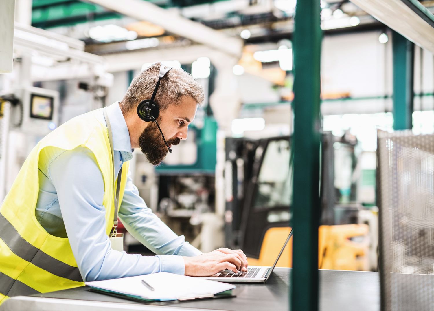 A worker using a laptop on the floor of a manufacturing plant